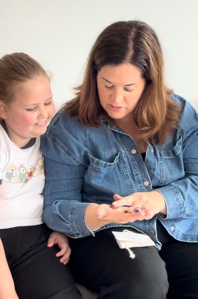 Woman and young girl sitting together, looking at crystals in her hands against a plain background