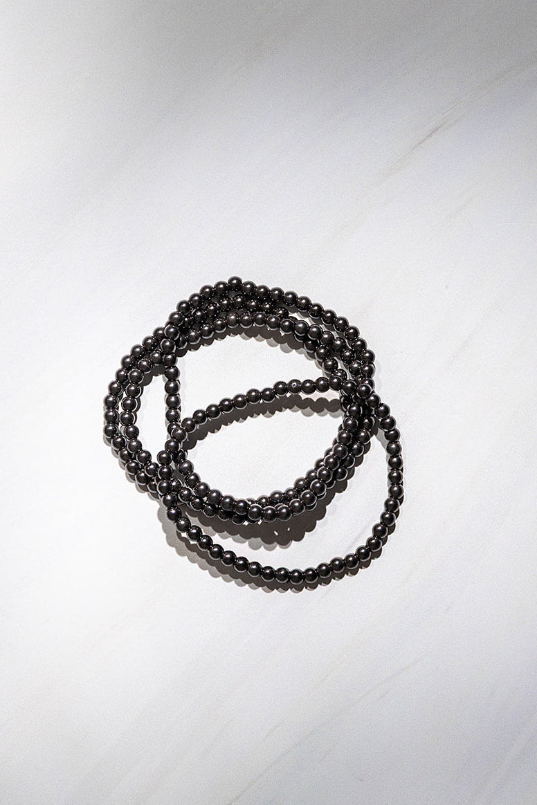 Multiple black magnetic hematite crystal bracelets coiled on a pale surface.