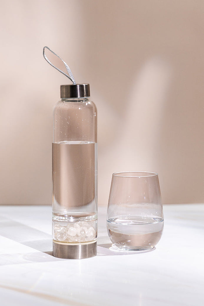 A crystal-infused glass water bottle beside a filled tumbler.